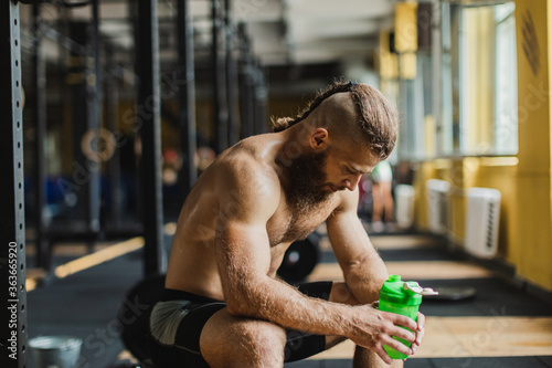 Strong and healthy man drinking water on a rowing machine, inside a crossfit gym.