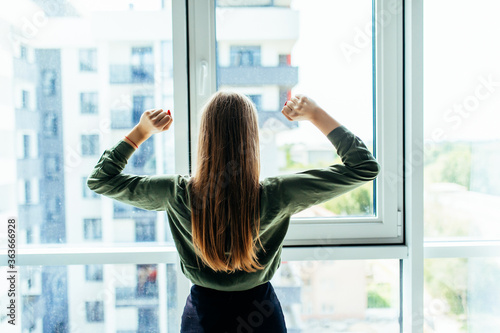 Rear view of young business woman with raised hands in front of window in office