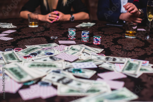 View of poker table with pack of cards  tokens  alcohol drinks  dollar money and group of gambling rich wealthy people playing poker