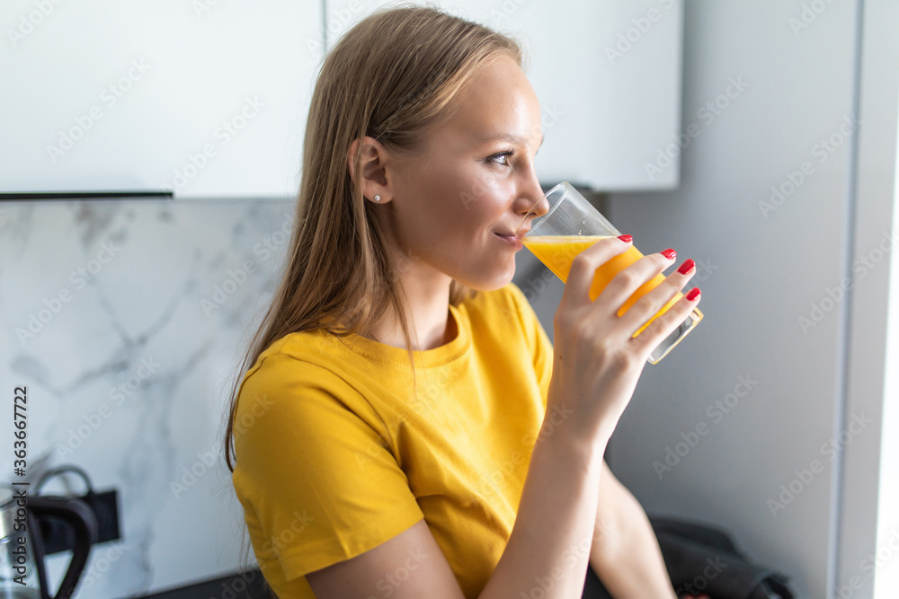 Attractive young woman holding a glass of orange juice while standing in the kitchen Attractive young woman holding a glass of orange juice while standing in the kitchen