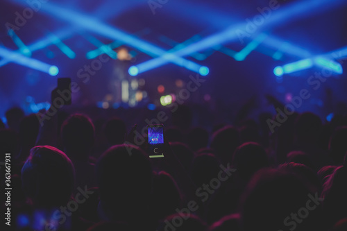 A crowded concert hall with scene stage lights, rock show performance, with people silhouette 