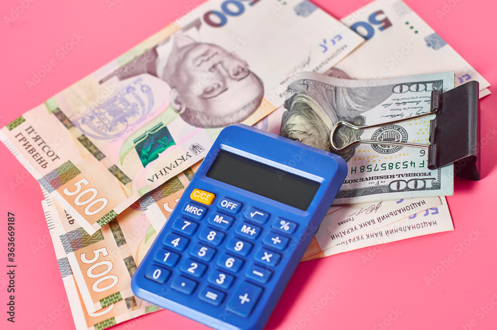 Banknote of one hundred dollars and ukrainian money near calculator on pink background Banknote of one hundred dollars and ukrainian money near calculator on pink background