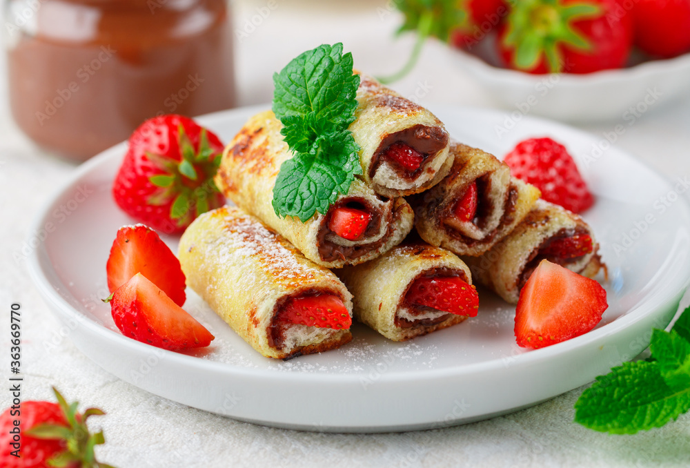 Rolls with chocolate and nut filling (Nutella), fresh strawberry berries, powdered sugar and mint. Delicious gourmet Breakfast. Selective focus Rolls with chocolate and nut filling (Nutella), fresh strawberry berries, powdered sugar and mint. Delicious gourmet Breakfast. Selective focus