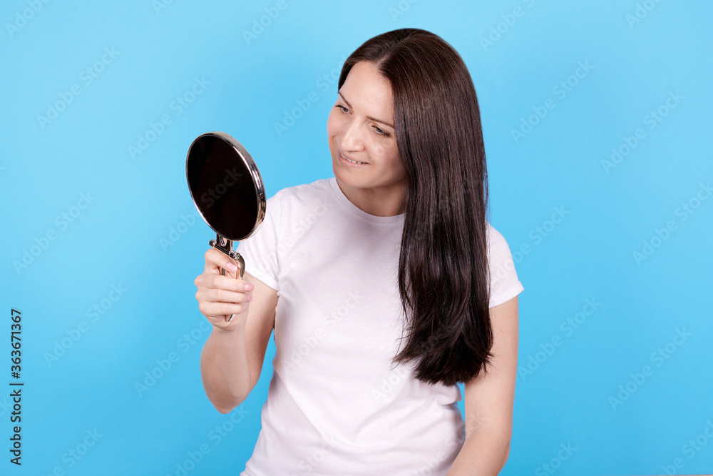 Girl looking at mirror and smiling. Isolated on blue background. Girl looking at mirror and smiling. Isolated on blue background.