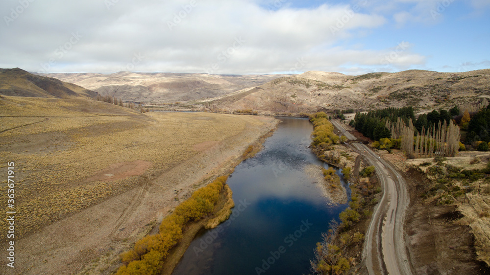Idyllic landscape. Traveling along the rural dirt road. Aerial view of a stream flowing across the golden meadow, valley and mountains. The sky reflection in the water. 