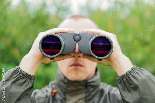 A young hunter in the forest looks into the binoculars. He is looking for wild animals.