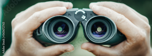 Banner close-up of a hunter man's hands holding binoculars on the blurred background.