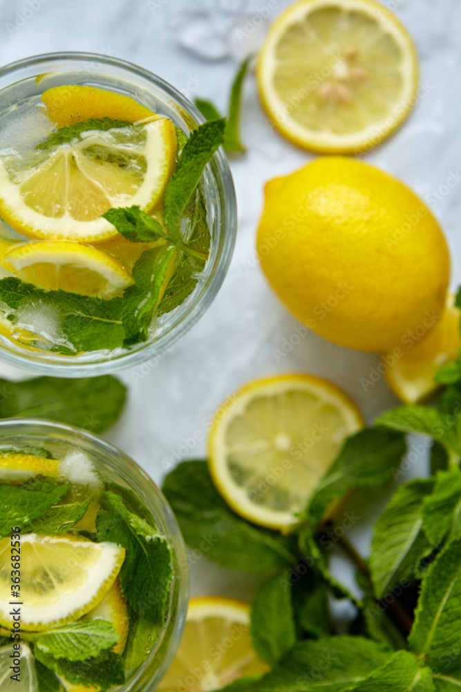 Refreshing drinks for summer, cold sweet and sour lemonade juice in the glasses with sliced fresh lemons. Refreshing summer drink. Traditional lemonade with lemon, mint and ice. Selective focus Refreshing drinks for summer, cold sweet and sour lemonade juice in the glasses with sliced fresh lemons. Refreshing summer drink. Traditional lemonade with lemon, mint and ice. Selective focus