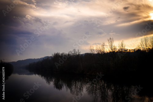 after sunset over the river with with bushes and trees and clouds in blue hour