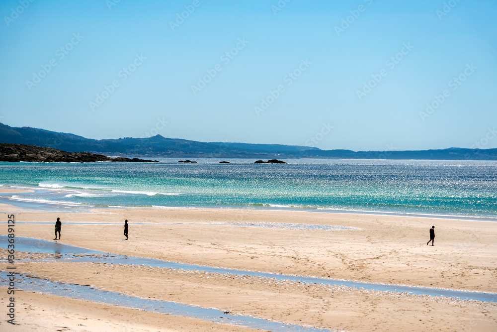 seascape of a beach in the atlantic ocean with fine sand and small silhouettes of people walking