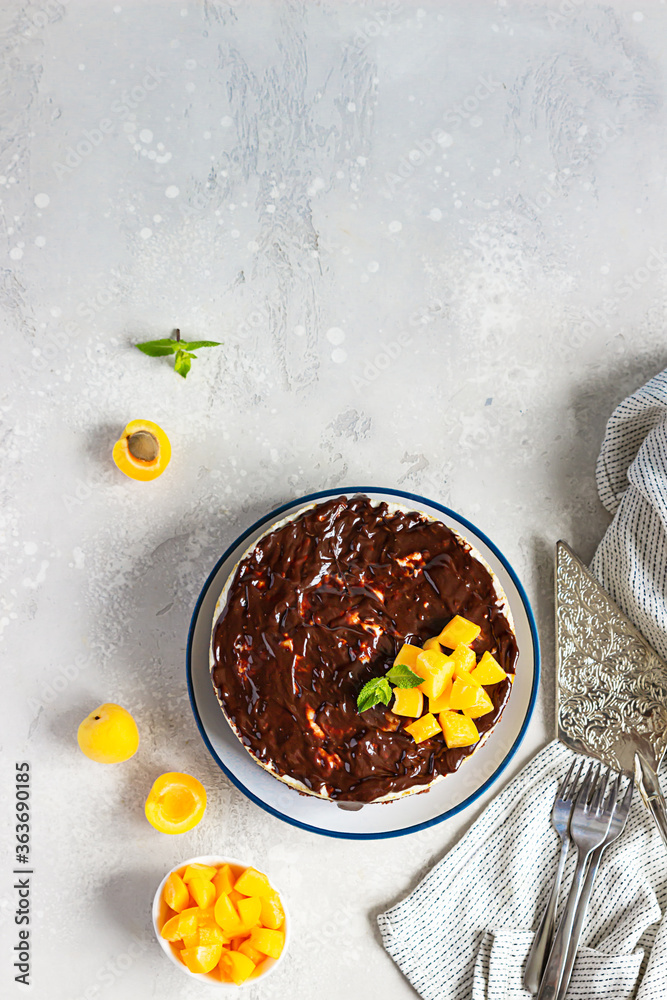 Fototapeta premium No bake apricot cheesecake decorated with chocolate glaze, fresh apricots and mint, light concrete background. Summer dessert. Copy space.