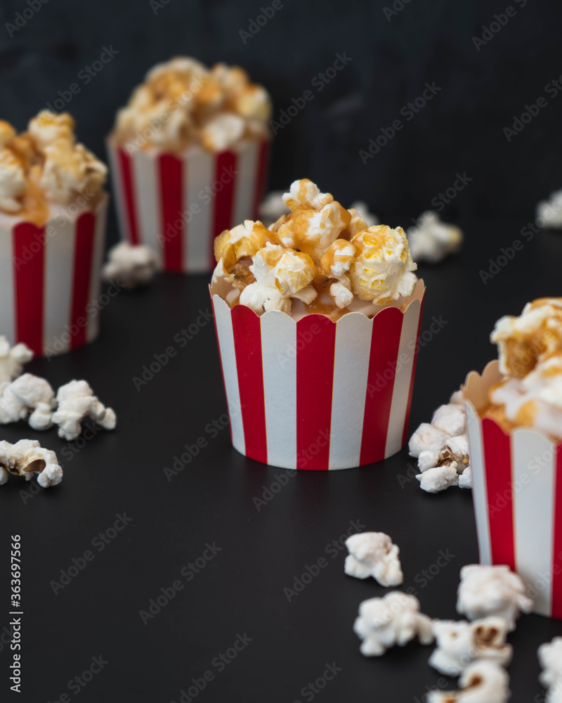 Movie night cinema style cupcakes in red and white containers with salted caramel sauce and topped with popcorn set against a black dark background