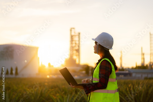 Asian woman petrochemical engineer working at night with laptop Inside oil and gas refinery plant industry factory at night for inspector safety quality control.. photo