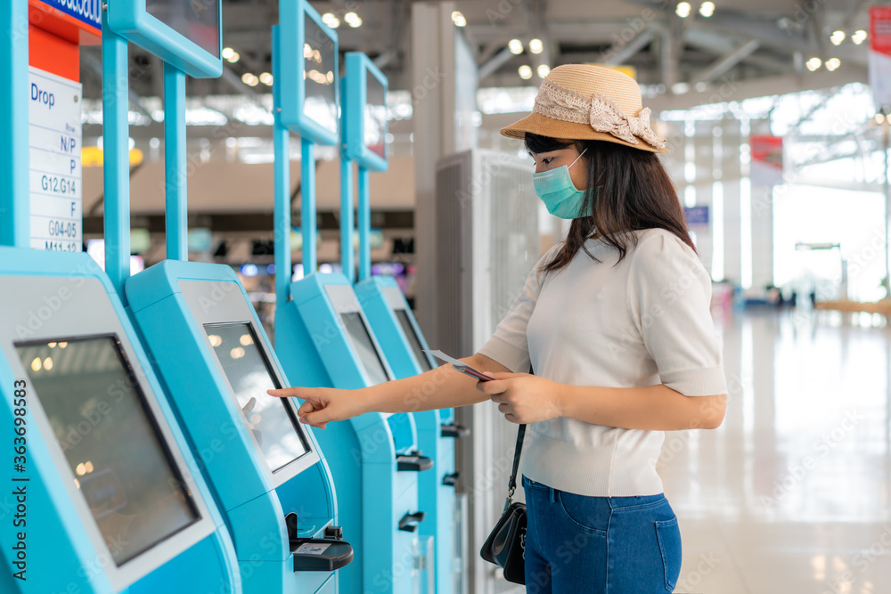 Asian woman traverler wearing mask using self check-in kiosk in airport terminal during coronavirus (COVID-19) pandemic prevention when travel abroad. New normal travel concept. Asian woman traverler wearing mask using self check-in kiosk in airport terminal during coronavirus (COVID-19) pandemic prevention when travel abroad. New normal travel concept.