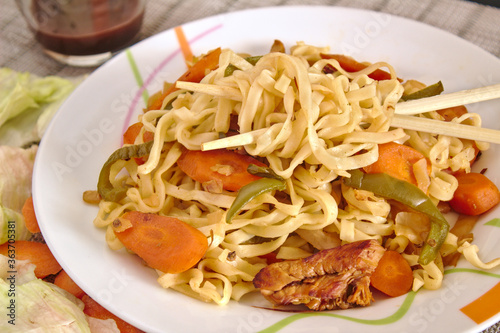 Side view of Chinese food that includes vegetables like carrots and lettuce with noodles, chicken and soy sauce. Delicious chicken meat