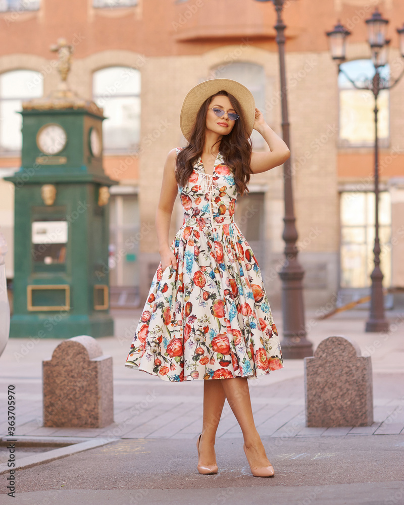 Young woman in colorful dress walking city street on a sunny summer day. Full length portrait. Elegant lady with long wavy hair. Girl in sunglasses