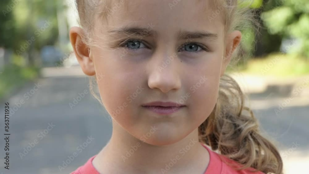 Portrait Little Child Girl Looking at Camera Standing on Street in City on Summer Day. Young Serious Thinking Curiosity Child Looking at Camera Closeup Outdoors. Face Eyes Serious Contemplative Child. Portrait Little Child Girl Looking at Camera Standing on Street in City on Summer Day. Young Serious Thinking Curiosity Child Looking at Camera Closeup Outdoors. Face Eyes Serious Contemplative Child.