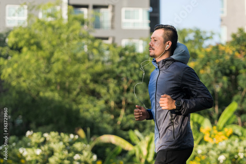 An athletic man in sport hoodie jogging in the city park in the evening after stressful work.