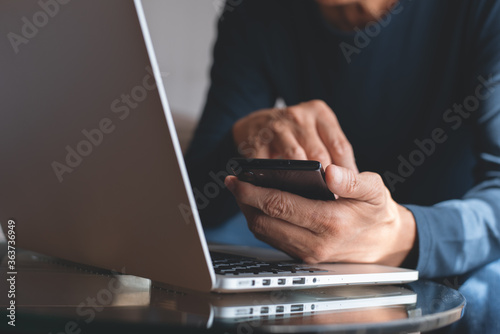 Man using mobile phone online working on laptop computer at home office