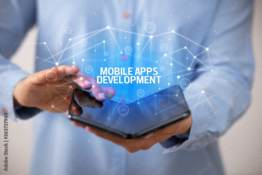Businessman holding a foldable smartphone with MOBILE APPS DEVELOPMENT inscription, new technology concept Businessman holding a foldable smartphone with MOBILE APPS DEVELOPMENT inscription, new technology concept