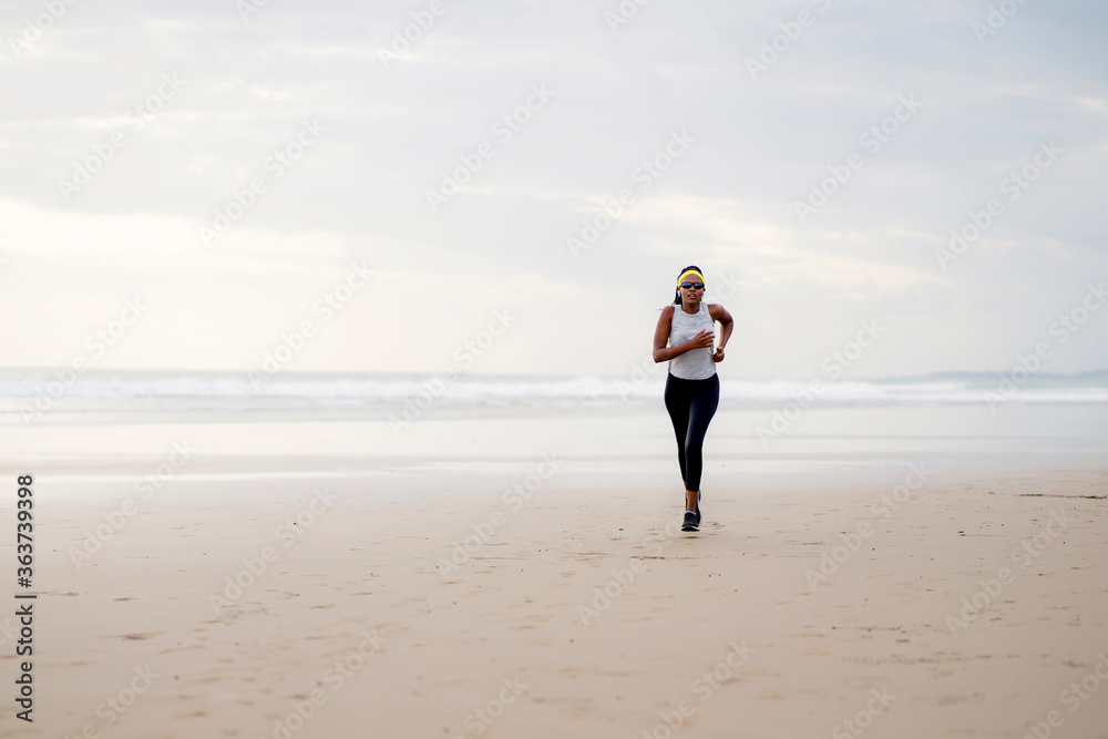 Afro American woman running on the beach - young attractive and athletic black girl training outdoors doing jogging workout at the sea in fitness and healthy lifestyle concept Afro American woman running on the beach - young attractive and athletic black girl training outdoors doing jogging workout at the sea in fitness and healthy lifestyle concept