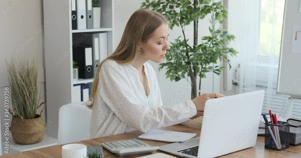 Businesswoman using laptop while calculating bills and writing notes at office Businesswoman using laptop while calculating bills and writing notes at office