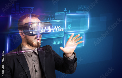 Businessman looking through Virtual Reality glasses with TECHNOLOGY IMPLEMENTATION inscription, new technology concept