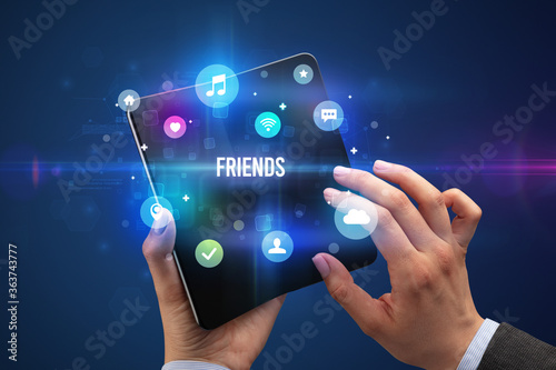 Businessman holding a foldable smartphone with FRIENDS inscription, social media concept