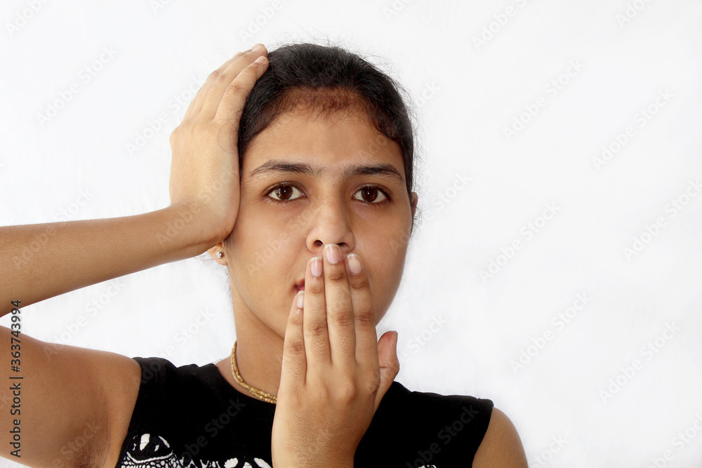 Portrait of amazed young woman, covering her mouth by hand and touching her head over on white background
