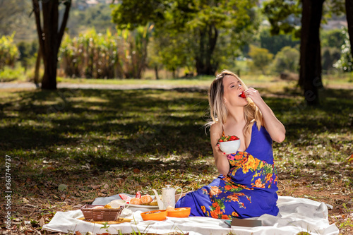 Young woman outdoors under trees in a park, happy and smiling, doing pic nic and tasting strawberries. photo