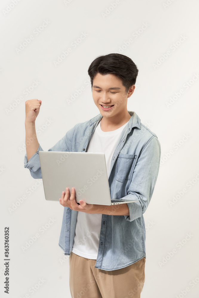 Happy young Asian man carrying laptop computer and raising his fist doing yes gesture isolated on white background Happy young Asian man carrying laptop computer and raising his fist doing yes gesture isolated on white background
