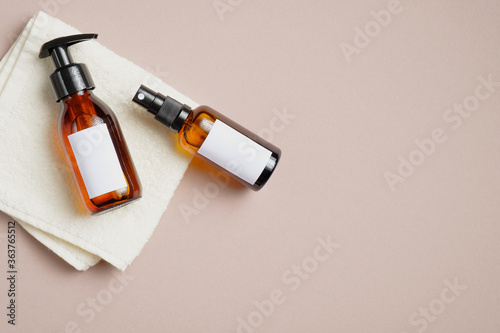 Amber glass bottle with shampoo and body spray on towel on beige background. Flat lay, top view, overhead. Cosmetic packaging mockup.
