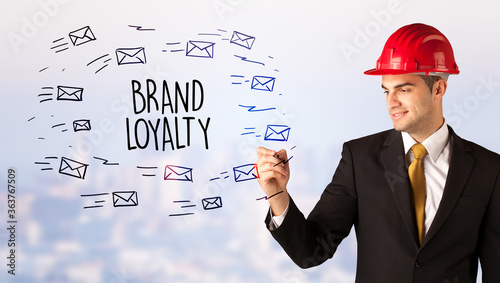 Handsome businessman with helmet drawing BRAND LOYALTY inscription, contruction sale concept