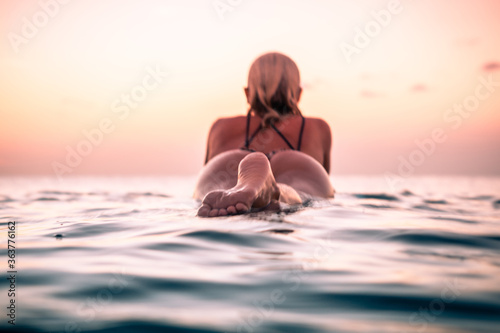 Portrait from the water of surfer girl with beautiful body on surfboard in the ocean at colourful sunset time © Lila Koan
