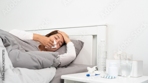 Sick Asian woman with cold sleeping on bed at home with high fever suffering from insomnia and medicine in foreground