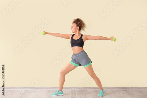 Sporty young woman training against light wall