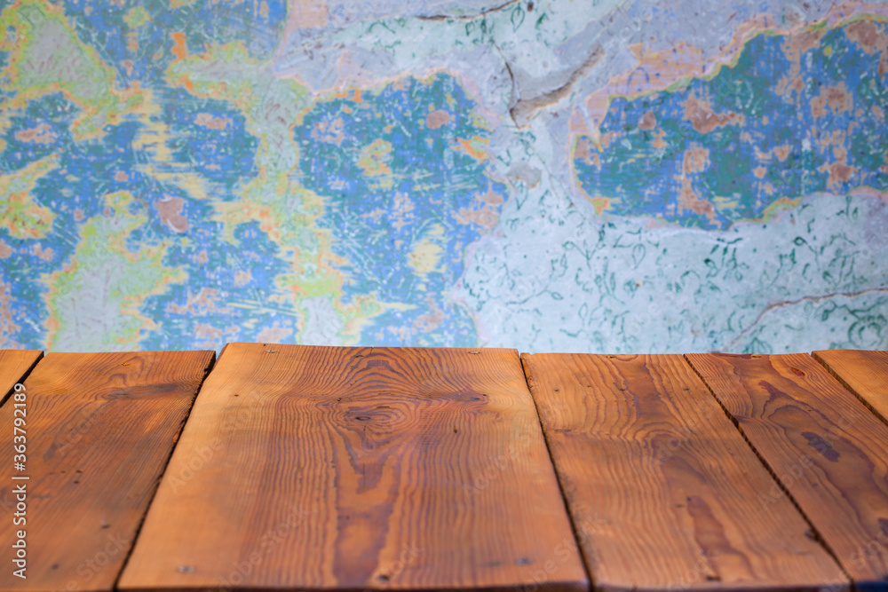 Pusty blat drewnianego stołu zbitego ze starych desek, w tle obdrapana wielokolorowa ściana, pomalowana farbą kredową. - obrazy, fototapety, plakaty 