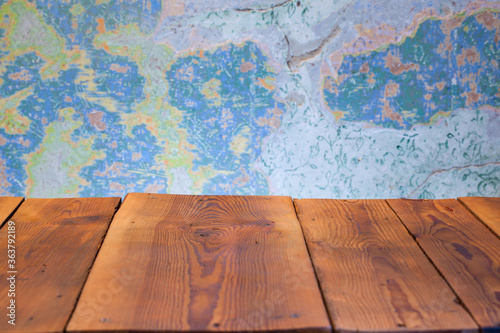Pusty blat drewnianego stołu zbitego ze starych desek, w tle obdrapana wielokolorowa ściana, pomalowana farbą kredową.