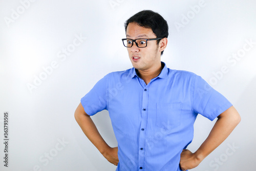 Young Asian Man wear blue shirt is funny angry face with shouting and pointing finger at camera isolated over white background