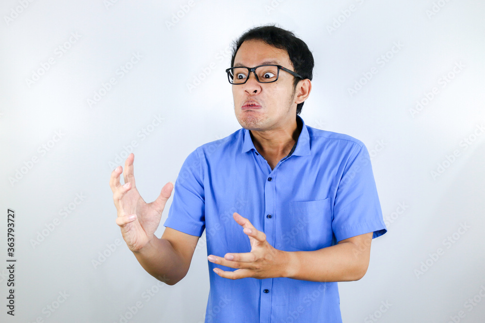 Young Asian Man wear blue shirt is funny angry face with shouting and pointing finger at camera isolated over white background