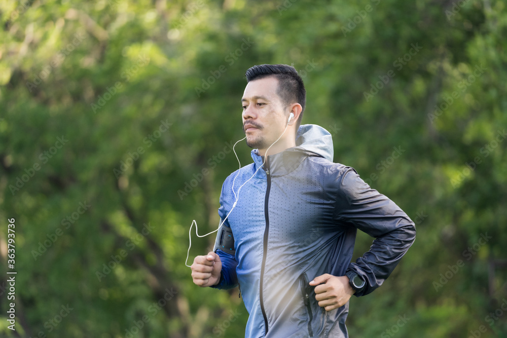 A man in sport hoodie jogging in the city park in the evening after stressful work. Runner jogging training and workout exercising power walking outdoors in forest city. Stock photo