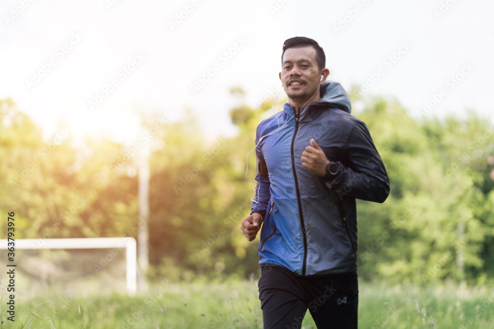 Obraz premium A man in sport hoodie jogging in the city park in the evening after stressful work. Runner jogging training and workout exercising power walking outdoors in forest city. Stock photo