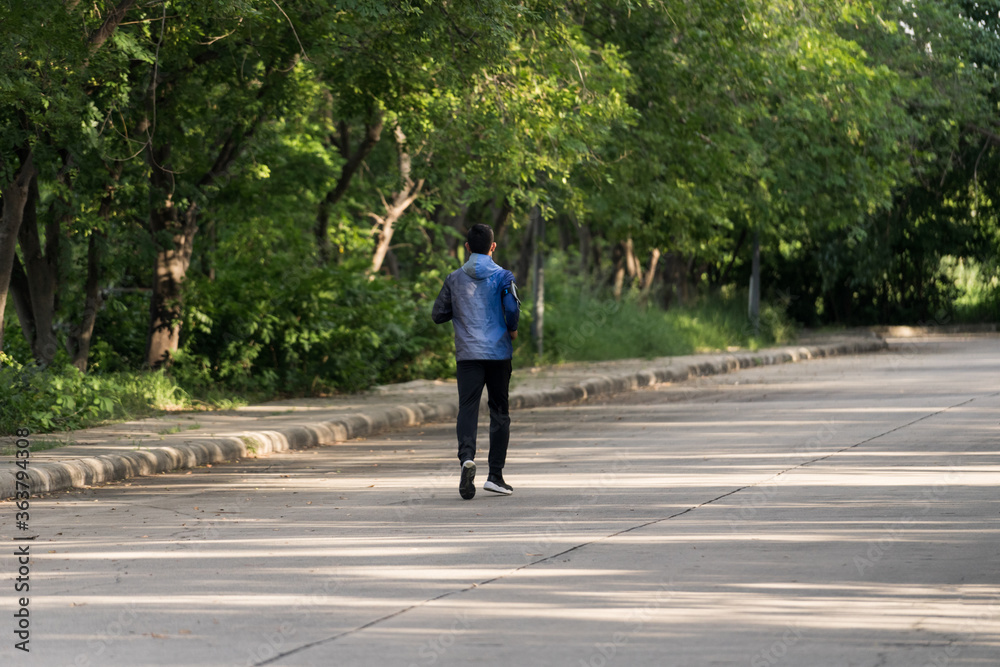 A man in sport hoodie jogging in the city park in the evening after stressful work. Runner jogging training and workout exercising power walking outdoors in forest city. Stock photo