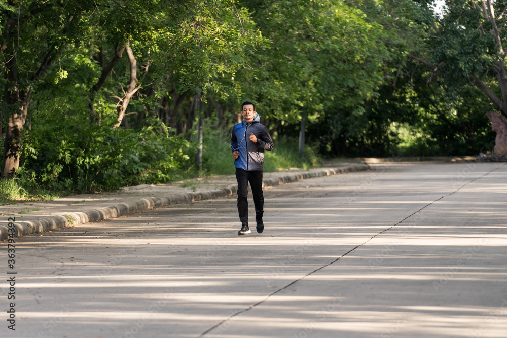 A man in sport hoodie jogging in the city park in the evening after stressful work. Runner jogging training and workout exercising power walking outdoors in forest city. Stock photo