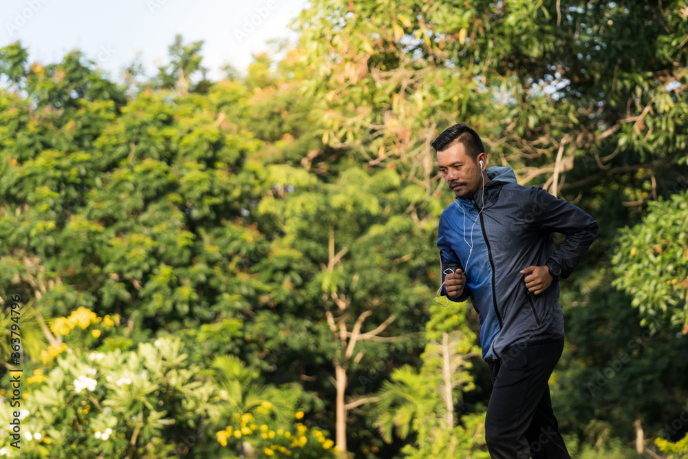 A man in sport hoodie jogging in the city park in the evening after stressful work. Runner jogging training and workout exercising power walking outdoors in forest city. Stock photo A man in sport hoodie jogging in the city park in the evening after stressful work. Runner jogging training and workout exercising power walking outdoors in forest city. Stock photo