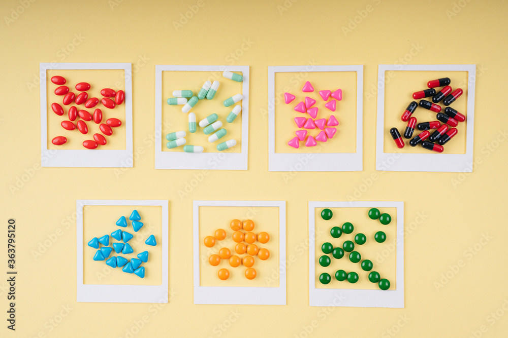 Colourful pills in white frame over yellow background.