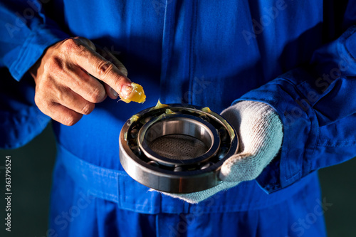 Mechanic is putting lubricant grease into ball bearing in a factory. photo