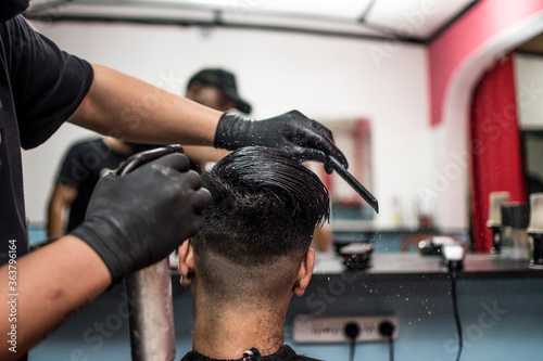man is doing a modern haircut in barbershop. Barber spray moistens hair.