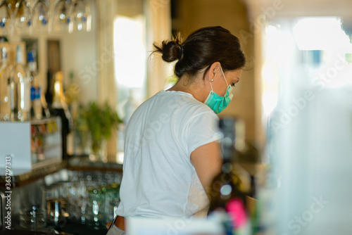 female barista at work wearing surgical portection face mask to prevent virus contagion , selective focus , bokeh photo