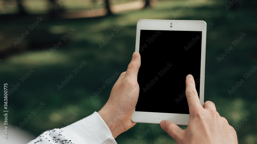 Close up view of young blogger hands holding and use white tablet pc for seeking collaboration with advertisers. Male surfing the internet while waiting for a work colleague. Mock up of gadget.